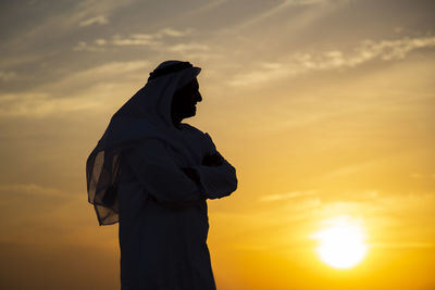 Side view of man in traditional clothing standing against sky during sunset