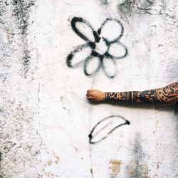 Optical illusion of cropped tattooed hand holding graffiti flower on wall