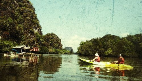 Men sitting on boat sailing in river against sky