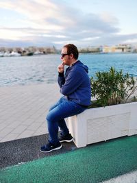 Young man photographing while sitting on sea against sky