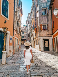 Young woman in white dress walking in old town street.