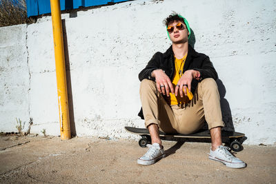 Portrait of young man sitting against wall