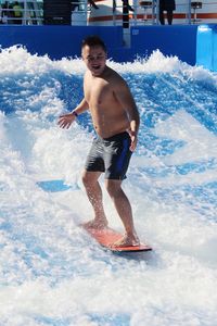 Full length of shirtless young man surfing in swimming pool