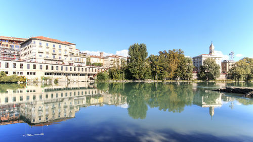 Scenic view of dora baltea river in city against clear blue sky