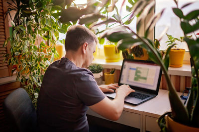 Man works with laptop remotely from home. distant work place with green-nature inspired home office