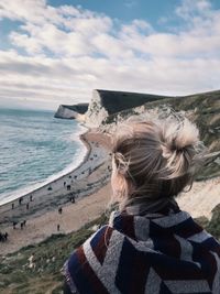 Rear view of woman on mountain by beach against sky