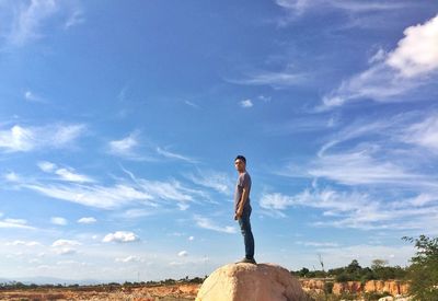 Side view full length of man standing on rock against blue sky