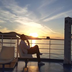 Man sitting on seat by sea against sky during sunset