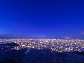 Aerial view of illuminated cityscape against blue sky