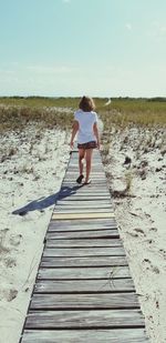 Rear view of girl walking on boardwalk against sky