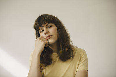 Young woman with hand on chin in front of white wall