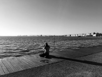 Rear view of man on pier over sea against clear sky