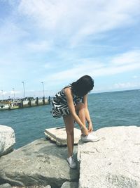 Woman standing on retaining wall by sea against sky