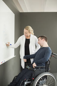 Businesswoman writing on whiteboard while working with disabled businessman in office