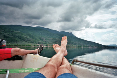 Low section of man relaxing on mountain against sky