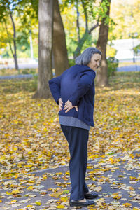 Full length of senior woman suffering from backache while standing outdoors