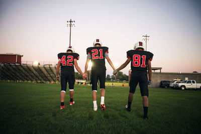 Rear view of male players holding hands and walking on field