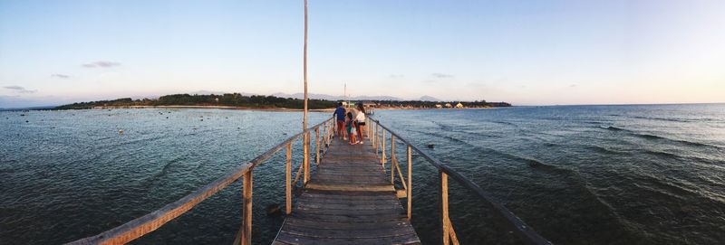 Family on pier over sea against sky