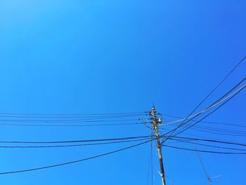 Low angle view of electricity pylon against clear blue sky during sunny day