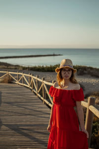 Portrait of young woman standing at beach against sky