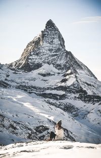 Woman sitting on snowcapped mountain against sky