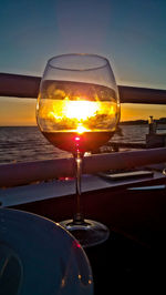 Close-up of wineglass against sky during sunset