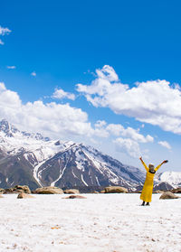 Rear view of woman standing on snow covered mountain against blue sky