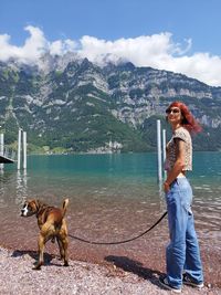 Side view of young woman with dog standing by sea against sky