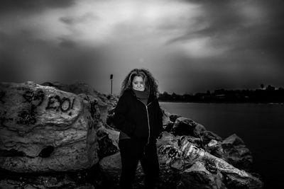 Portrait of young woman standing on rock against sky