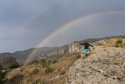 One man trail running on a rock under a rainbow