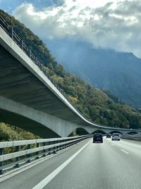 Cars on road by bridge against sky