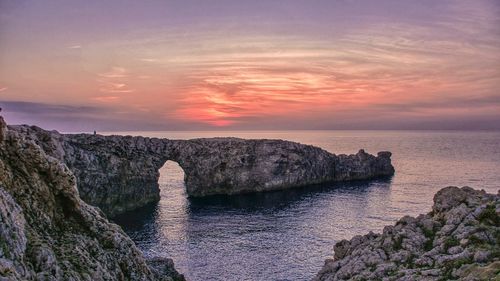 Rock formation in sea against sky during sunset