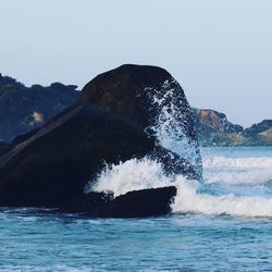 Sea waves splashing on rocks against clear sky