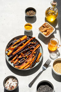 Baked glazed spicy violet and orange carrots with ingredients on grey background. top view