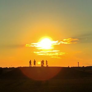 Silhouette people standing on landscape against orange sky