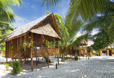 Chairs and palm trees on beach by house against sky