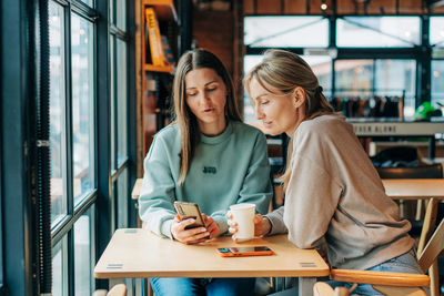 Two modern women make purchases on websites using a mobile phone.