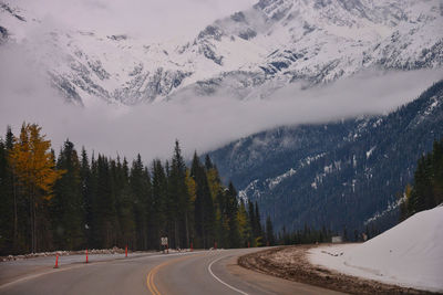 Road amidst trees and snowcapped mountains against sky during winter