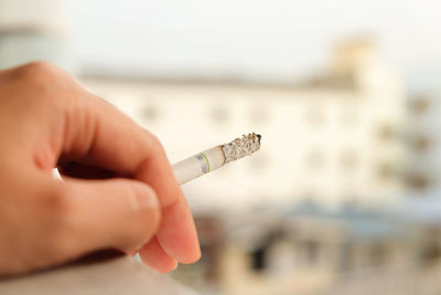 Cropped hand holding cigarette against buildings