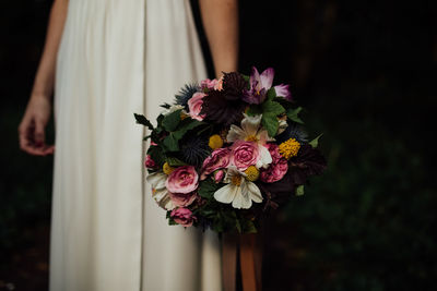 Midsection of woman holding bouquet while standing against black background