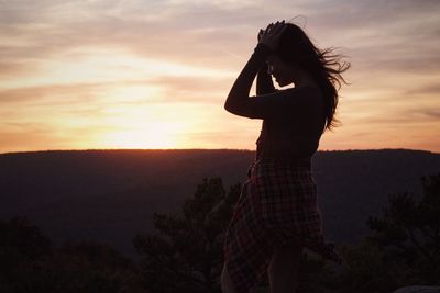 Woman standing by silhouette palm tree against sky during sunset