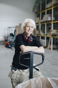 Portrait of smiling mature woman leaning on pallet jack at industry