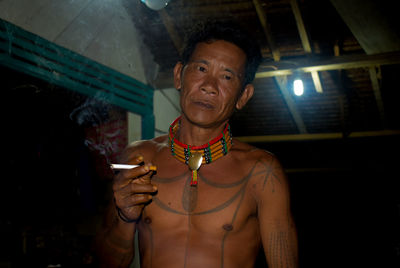 Portrait of shirtless man smoking cigarette in darkroom