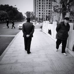 Rear view of people walking on footpath in city