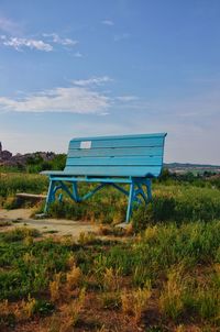 Empty bench on field against sky