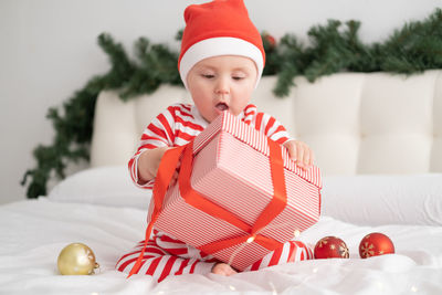 Cute baby girl holding christmas gift on bed