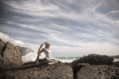 Man sitting on rock by sea against sky