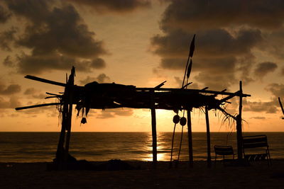 Silhouette cranes on beach against sky at sunset