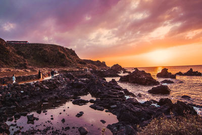 Rocks on shore against sky during sunset