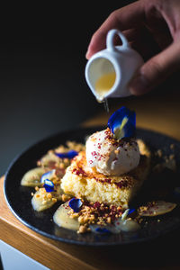 Cropped hand pouring syrup on dessert at table